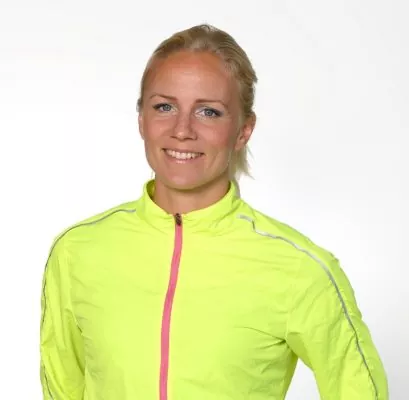 Person som bär en ljusgul atletisk jacka med rosa dragkedja, ler och poserar mot en vanlig vit bakgrund.