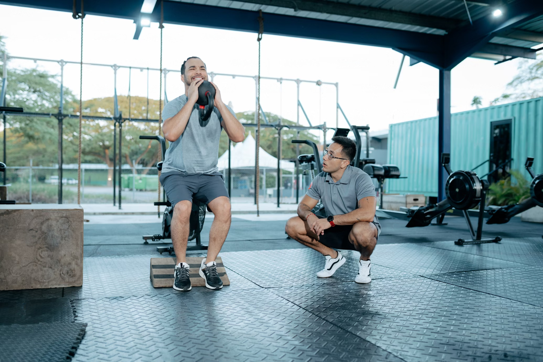 En person utför en knäböj med en vikt, medan en instruktör övervakar dem i ett gym.